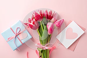 Top view photo of bouquet of fresh tulips tied with ribbon blue present box and envelope with letter on pastel pink background