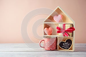 Mother`s day concept with toy house, coffee cup. gift box and heart shapes on wooden table