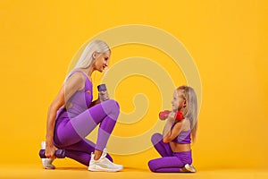 Mother`s day concept. Young mother and daughter exercise together with dumbbells. Family look.