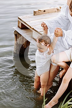 Mother& x27;s day. cropped photo legs of mom and two child daughters sitting on wooden bridge by the lake, pond and