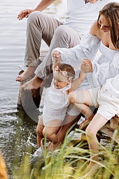 Mother& x27;s day. cropped photo legs of mom and two child daughters sitting on wooden bridge by the lake, pond and