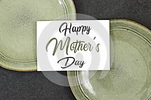 Mother\'s Day decorations concept. Top view photo of white invitation card with green ceramic plate.