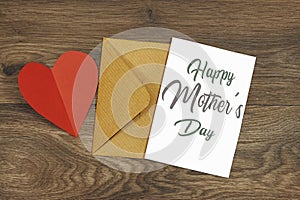 Mother\'s Day decorations concept. Top view photo of white invitation card with red heart shape paper on wood table.