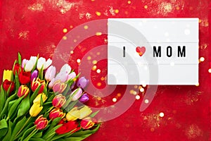 Mother`s day greeting card. Colorful tulips bouquet on red background and I LOVE MOM written on light box. Mother`s day