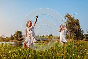 Mother`s day. Happy girls running with kite in summer park while mother helps them. Children having fun playing outdoors