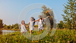 Mother`s day. Happy girls running with kite in summer park while mother helps them. Children having fun playing outdoors