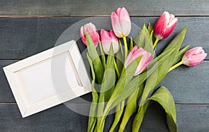 Mother`s day. Pink tulips and a white blank frame on blue background, copy space, top view