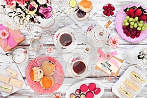 Mothers Day tea table scene over a white wood background. Greeting card, gift, flowers, vintage tea set, finger sandwiches, choco