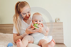 Mother`s day. Young woman playing with her newborn baby son at home. Family having fun. Infant biting ball on bed