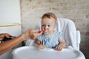 Mother`s hand feeding a young child from a red plastic spoon