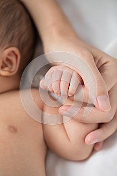 Mother`s hand holding infant baby boy`s hand with care.