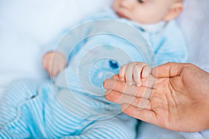 Mother`s hand holds a cute little baby in her hand at home on the bed