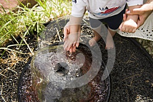 A mother's hands hold a boy's small hands in a decorative fountain