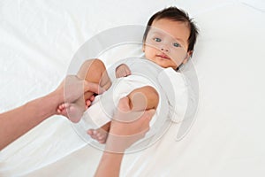 mother's hands holding baby legs and doing some playful exercises on bed