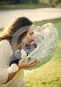 Mother`s love. Mother woman kiss baby son in basket on natural landscape