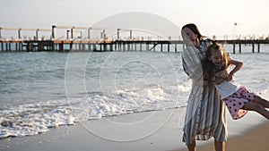 Mother the sandy beach is lacking a little daughter in his arms hugging and circling around him. Happy family.