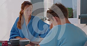 A mother scolds her teenage son while sitting at breakfast near the house. A woman speaks emotionally and scolds a