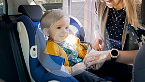 Mother seating and fastening safet car seat of her baby son