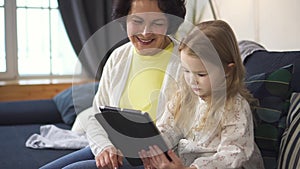 Mother is showing charming little girl laptop and control screen of tablet.