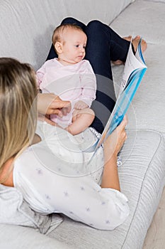 Mother showing story book to her baby in living room