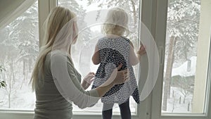 Mother is showing the winter landscape to her little daughter through a window