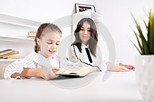 Mother sitting with baby girl and teaching her to read.