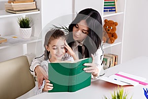 Mother sitting with baby girl and teaching her to read.