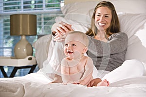 Mother sitting on bed with amused baby