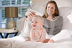 Mother sitting on bed with amused baby photo