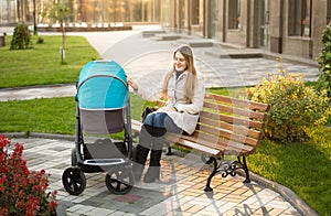 Mother sitting on bench at park and swaying baby stroller