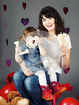 mother sitting on chair with baby girl toddler on her laps knees in studio holding wooden letters