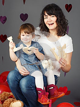 Mother sitting on chair with baby girl toddler on her laps knees in studio holding wooden letters love smiling laughing