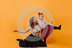 Mother sitting and her beautiful little daughter with two pigtails smiling and lifting a leg in new-year pull-overs.