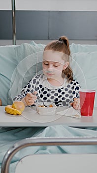 Mother sitting with sick child patient while eating healthy food lunch in hospital ward