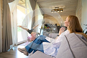 Mother sitting on sofa and looking her daughter performance