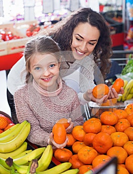 Mother and small cheerful daughter buying citrus fruits