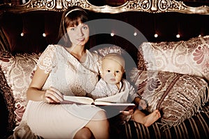 Mother with a small child in the interior reading a book together. Smiling family in the bedroom reading a book. Mom and baby on