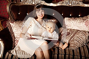 Mother with a small child in the interior reading a book together. Smiling family in the bedroom reading a book. Mom and baby on