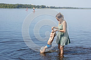 Mother with small child playing and having fun together on the beach. Happy family outdoors. Mom and baby at summer on nature