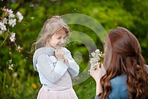 Mother with small daughter blowing to dandelion - lifestyle outdoors scene in park. Happy family concept