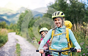 Mother with small daughter cycling outdoors in summer nature, looking at camera.