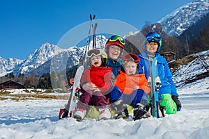 Mother with small kids sit in the snow wear ski outfit