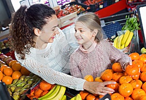 Mother and small pretty daughter buying citrus fruits