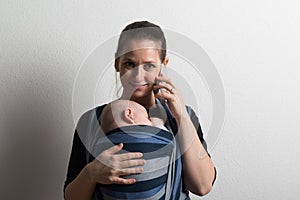 Mother with smartphone and baby sleeping in sling. Studio shot.