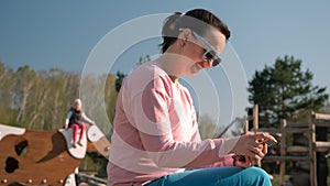 Mother with Smartphone Sitting at Playground