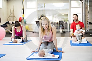 Mother smiling at baby while performing exercise above. Group exercise class, fitness or pilates for parents. Moms