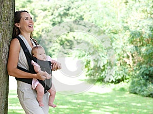 Mother smiling in park with baby in sling