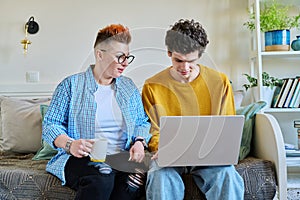 Mother and son 19-20 years old, sitting together on couch at home, looking at laptop screen