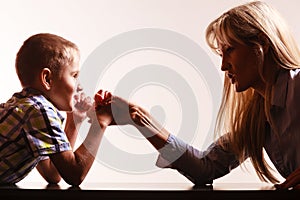 Mother and son arm wrestle sit at table.