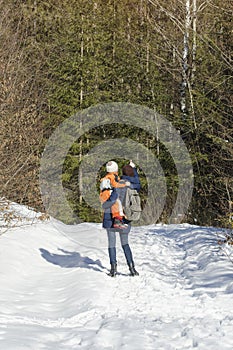 Mother with son in arms and backpack stands against the background of coniferous forest and snow-covered road. Winter day